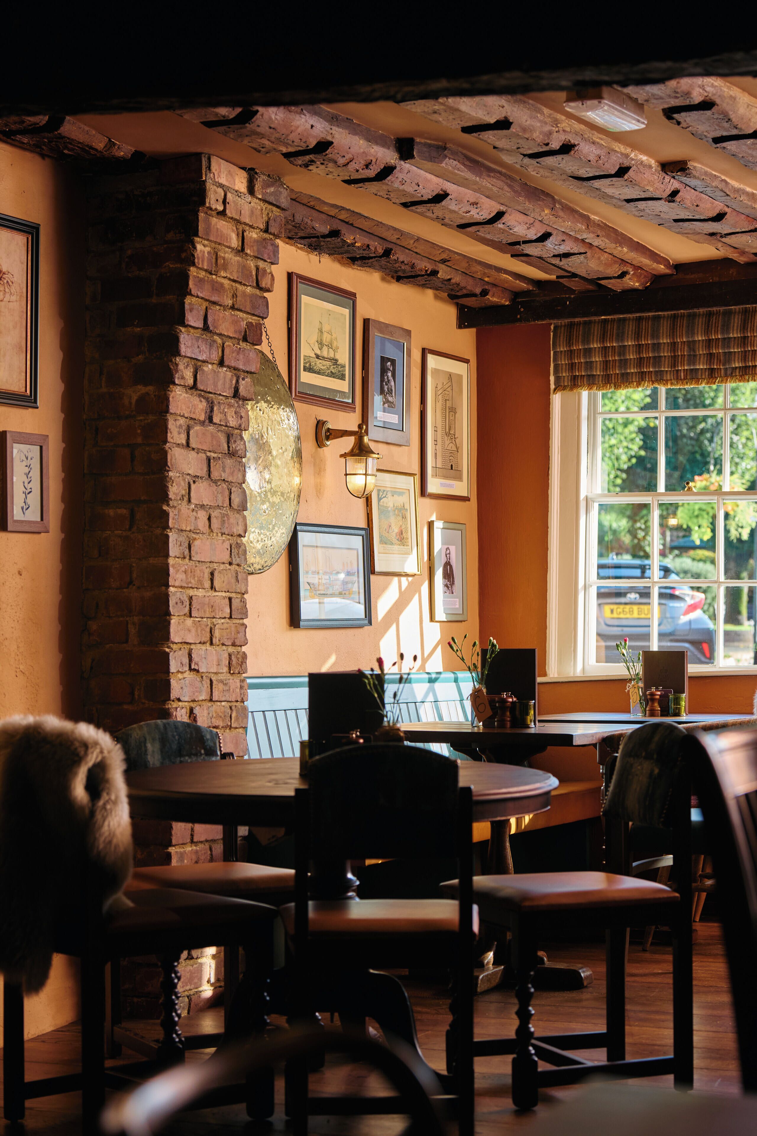 A cozy restaurant with brick walls, framed pictures, and a window with a view of the street.