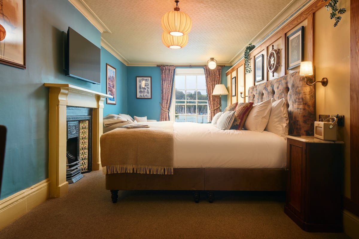 A bedroom with a large bed, a fireplace, a television, and a window with curtains.