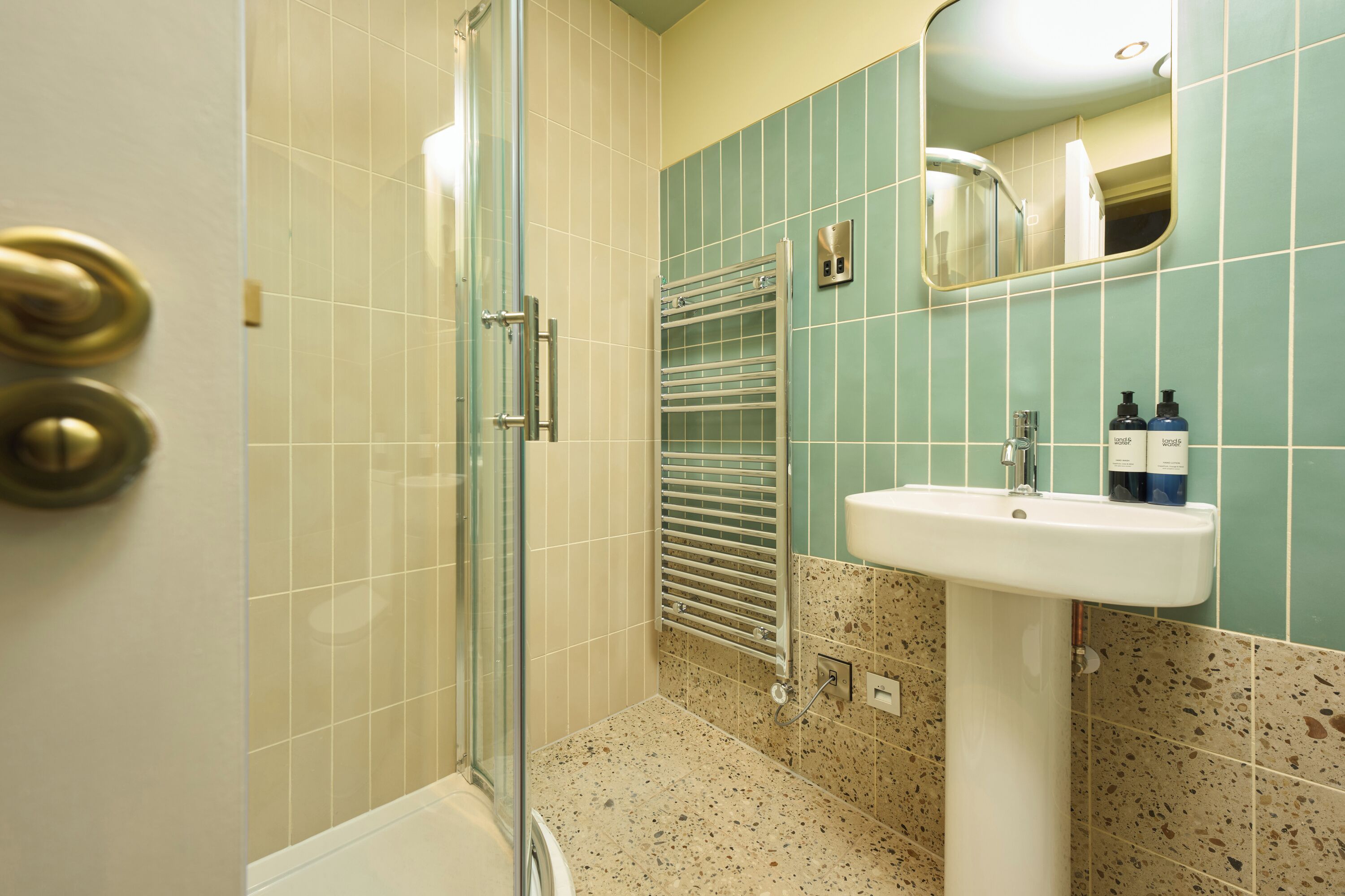 A bathroom with a glass shower enclosure, a sink with a mirror above it, and a towel rack.