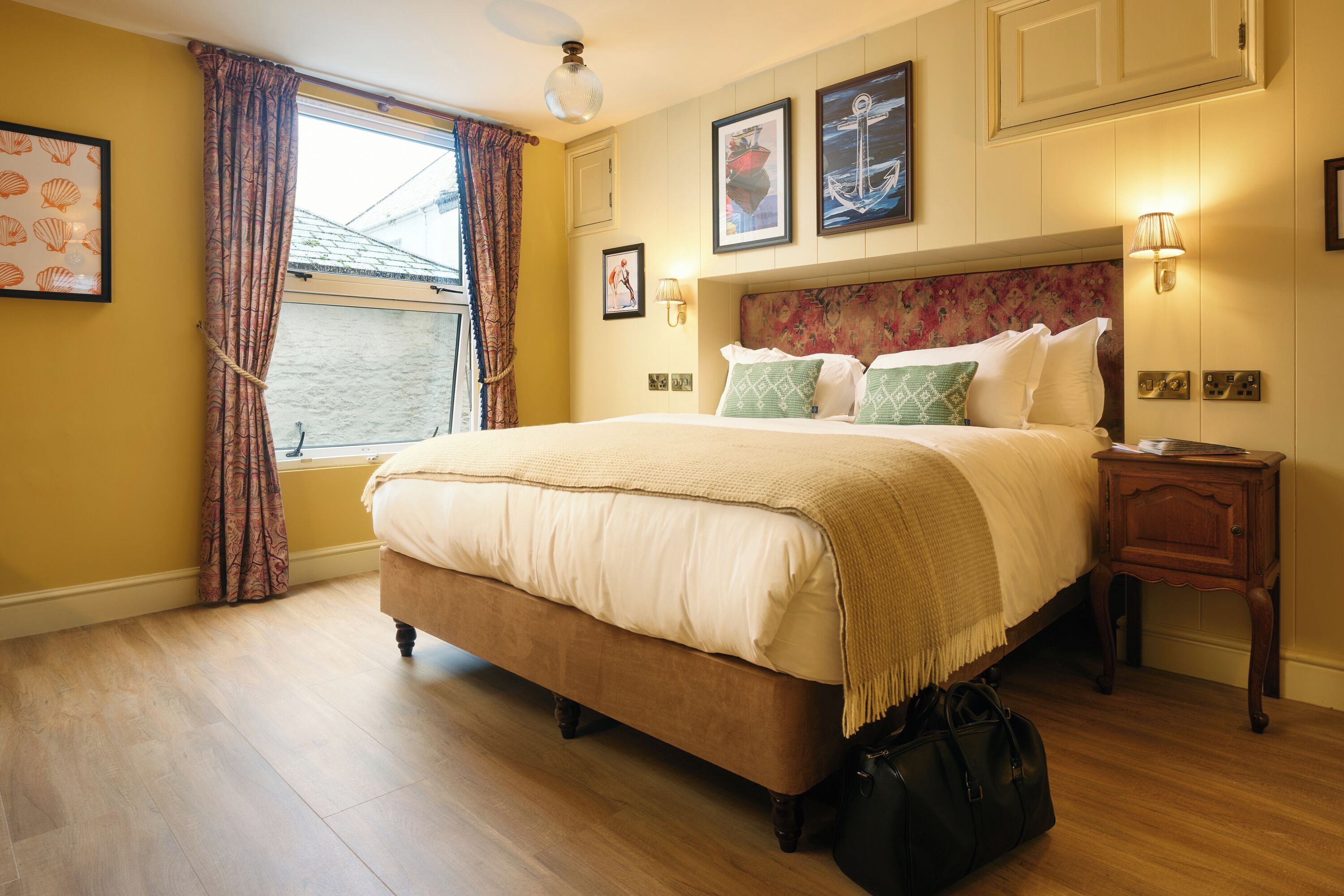 Habitación de hotel con una cama grande, una ventana con cortinas, cabecera con estampado floral y lámparas fijadas a la pared.