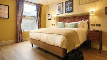 Habitación de hotel con una cama grande, una ventana con cortinas, cabecera con estampado floral y lámparas fijadas a la pared.
