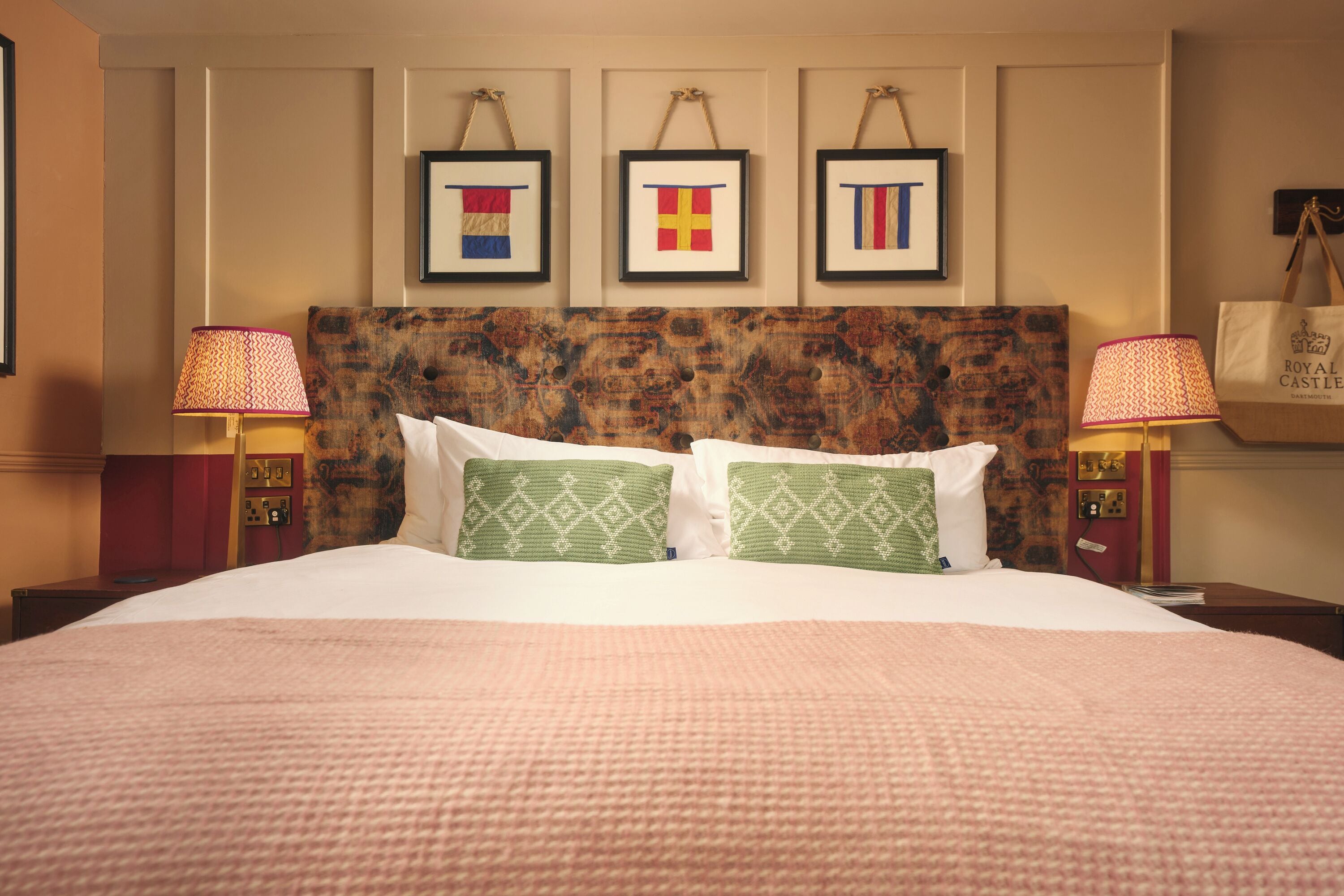 Ein Hotelzimmer mit einem großen Bett, zwei Nachttischlampen und drei gerahmten Kunstwerken an der Wand.