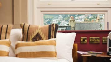 A hotel room with a bed, pillows, a desk, and a view of a town through a window.