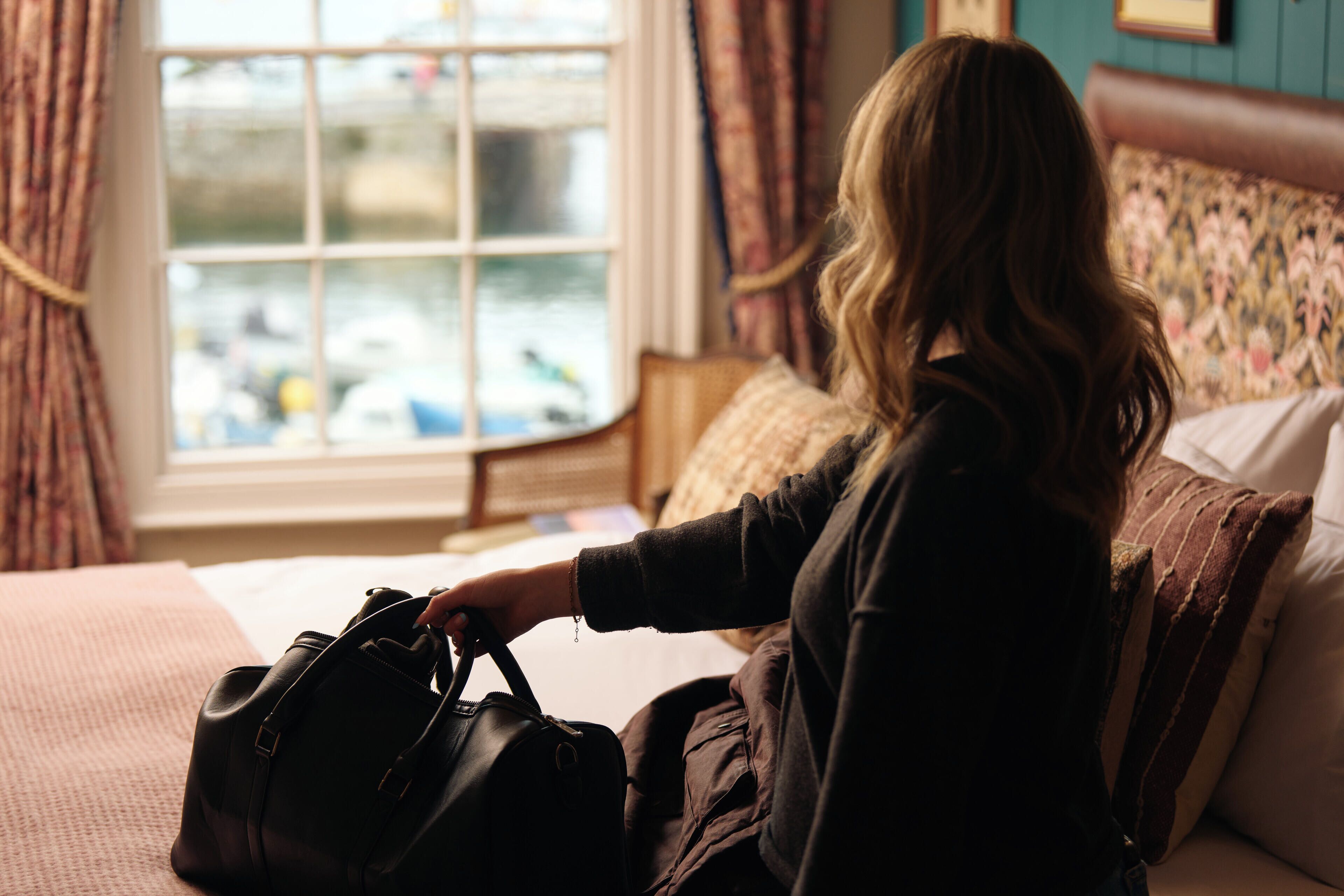 A person sitting on a bed with a window view of boats.