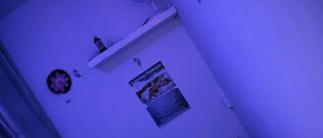 A room with a bed, a wall-mounted shelf with items, a poster, and a small fan.