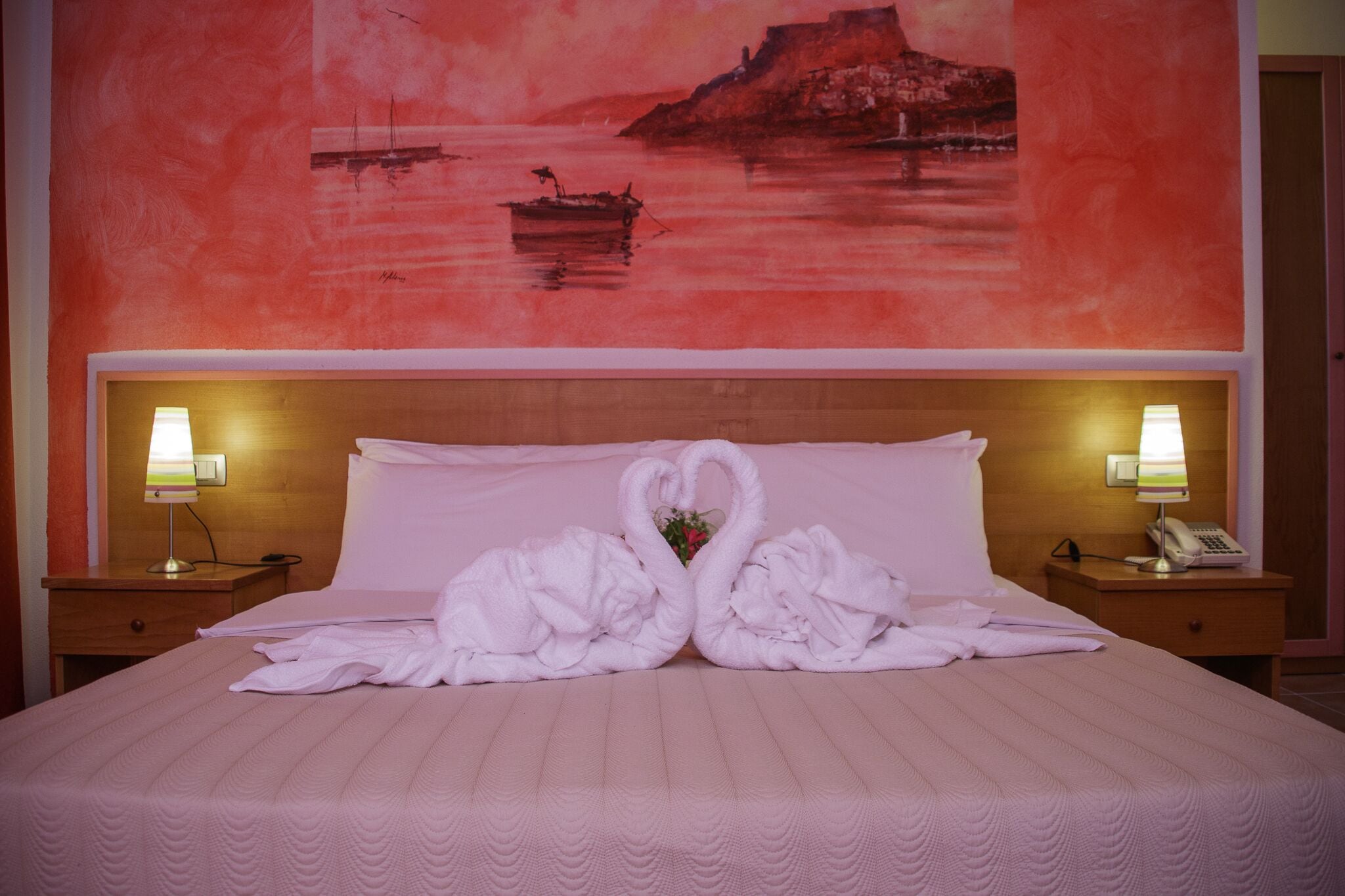 A hotel room with a bed, two bedside lamps, and a painting of a coastal scene.