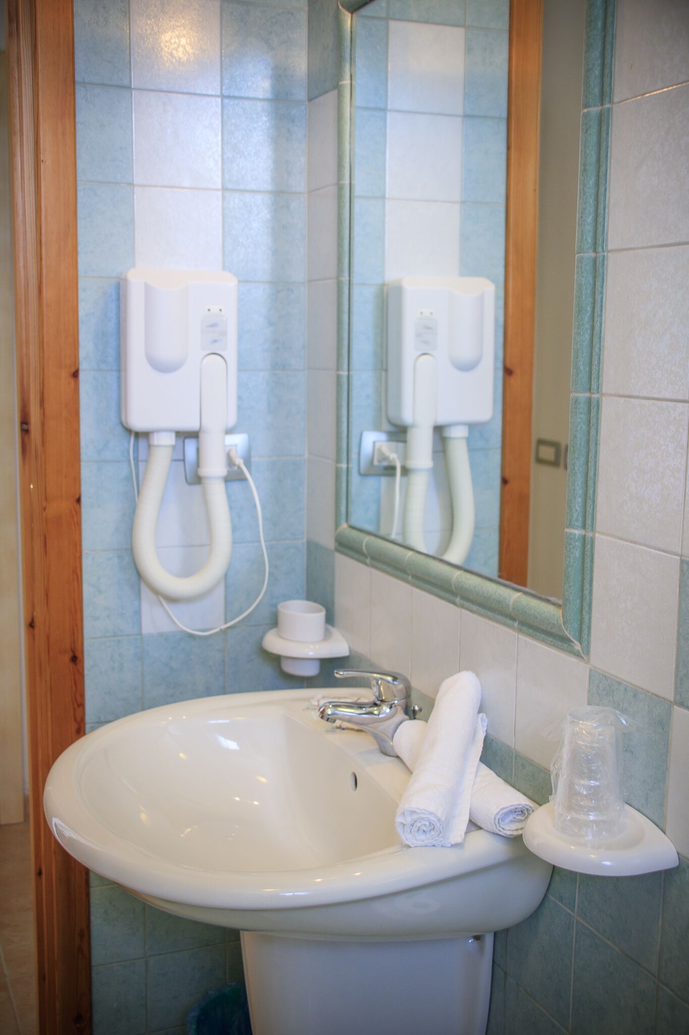A bathroom with a sink, mirror, and towel dispenser.