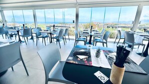 Un comedor moderno con mesas y sillas, ventanas amplias que ofrecen vistas al océano y al paisaje.