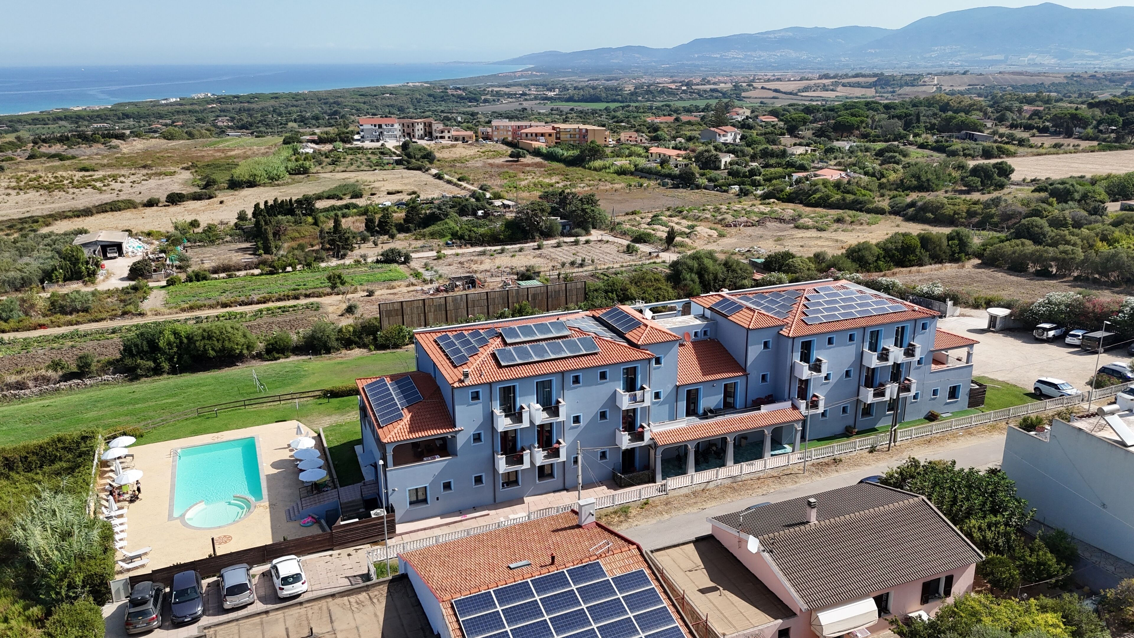 A multi-story building with solar panels on the roof, a swimming pool, and a parking area.