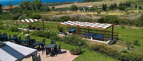 Un espacio al aire libre con mesas y sillas, una mesa de ping pong y vistas al mar y las colinas.