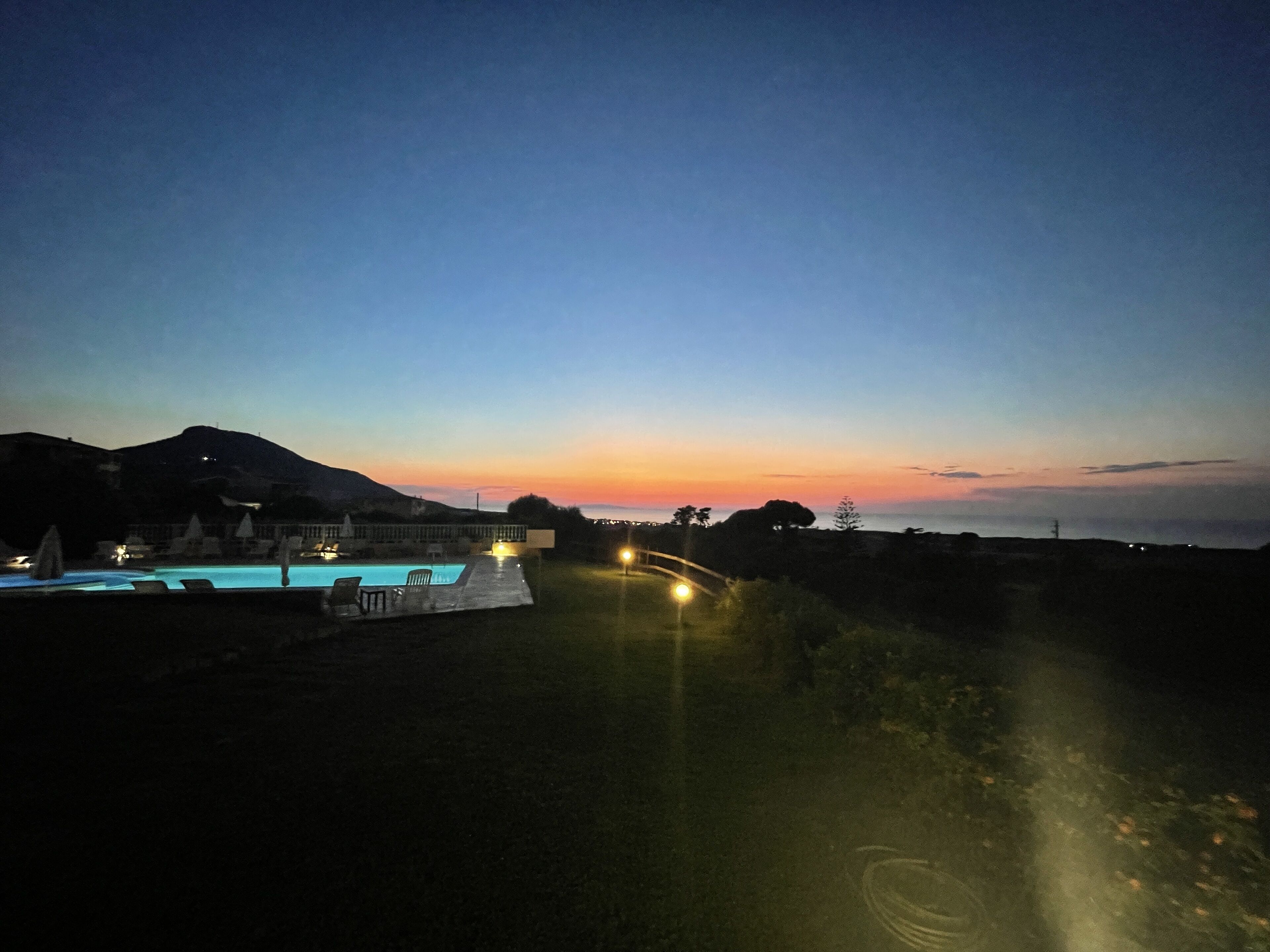 Un resort con piscina, sillas de descanso y vista al atardecer sobre el océano.