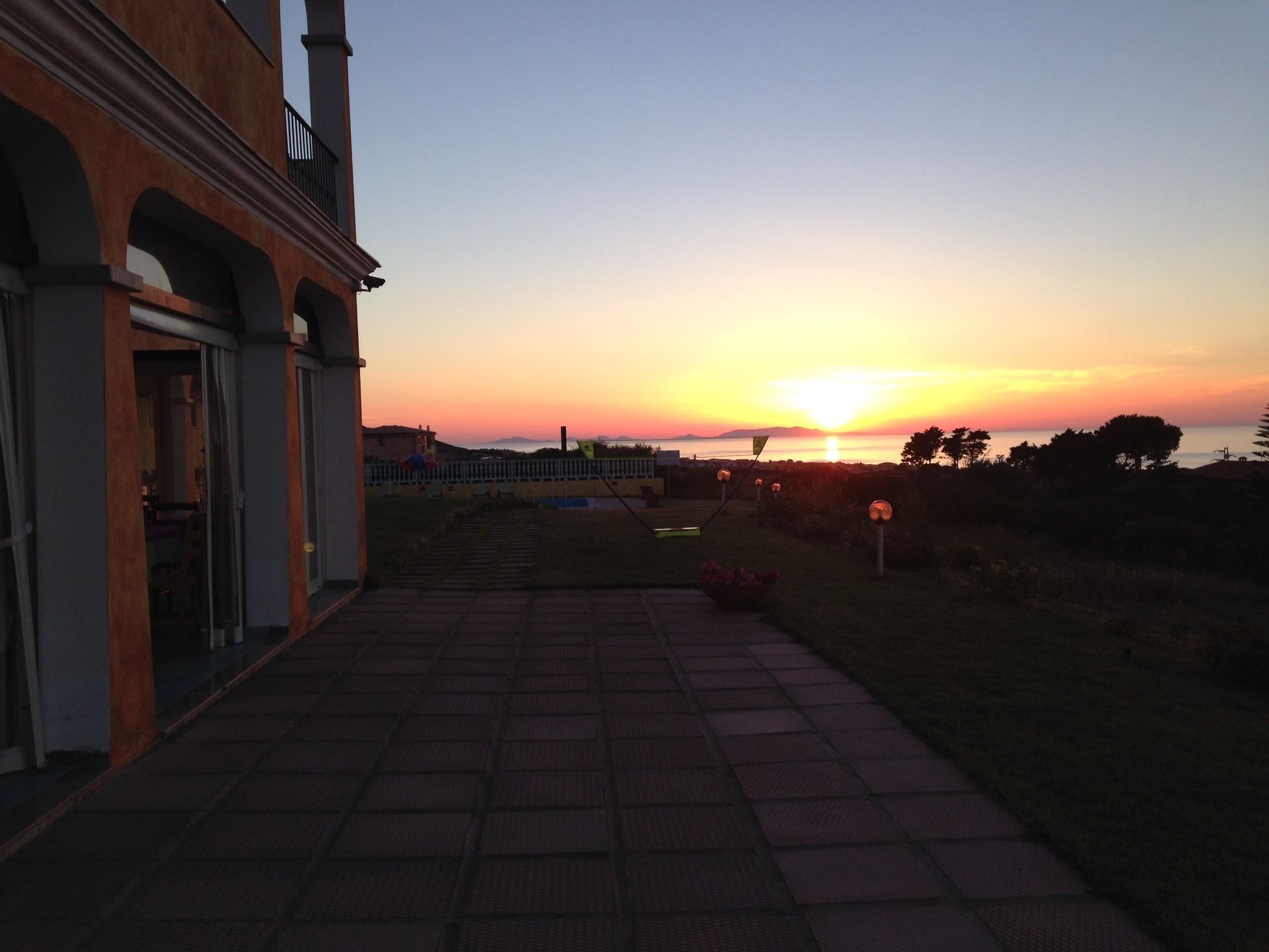 A paved pathway leading to a building with a view of the sunset over the sea.