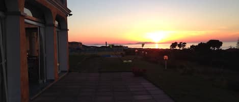 A paved pathway leading to a building with a view of the sunset over the sea.