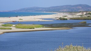 Una playa con agua cristalina, orilla de arena y montañas a lo lejos.