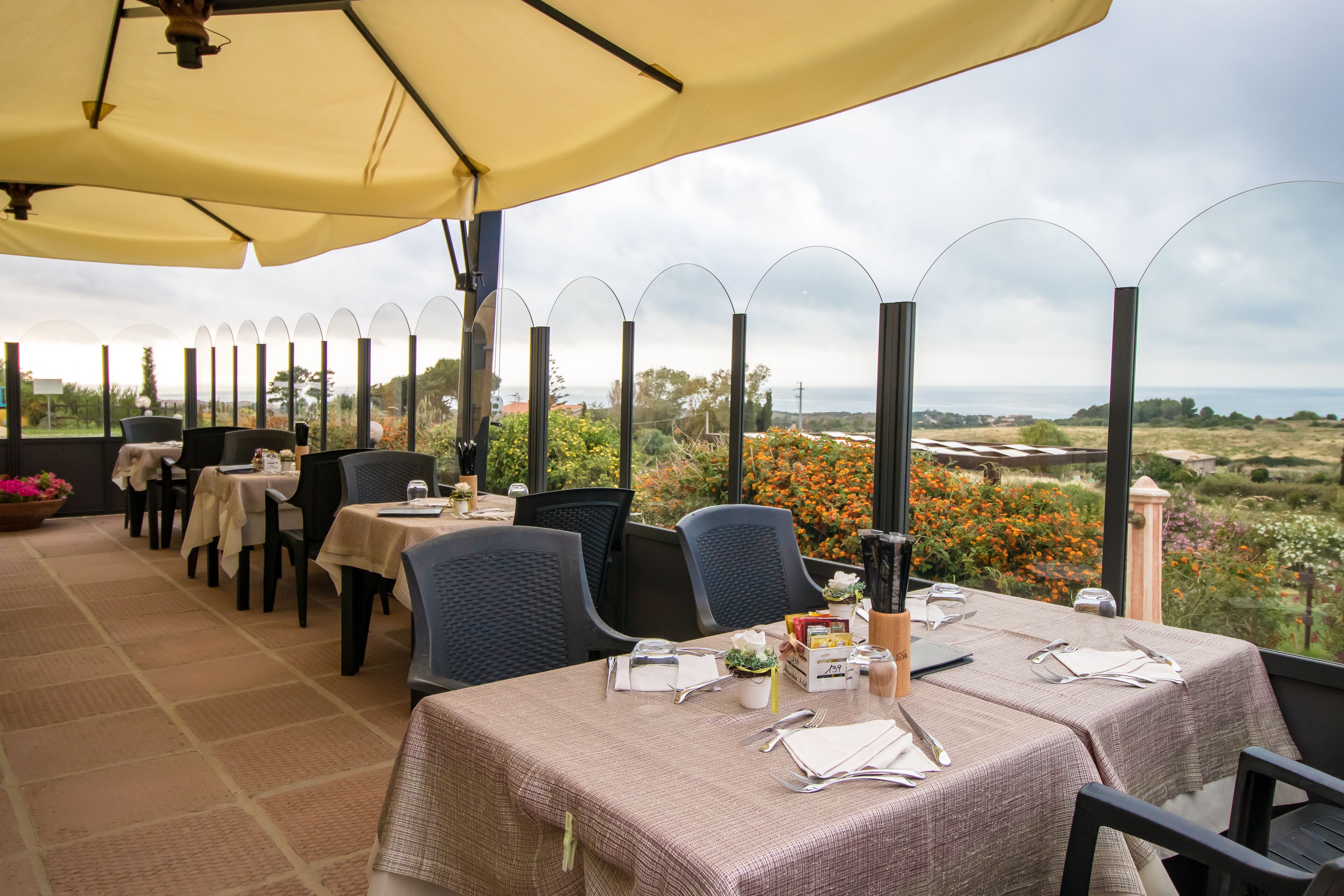 Un área de comedor al aire libre con mesas dispuestas para dos, cubierta por sombrillas, y vistas al campo.