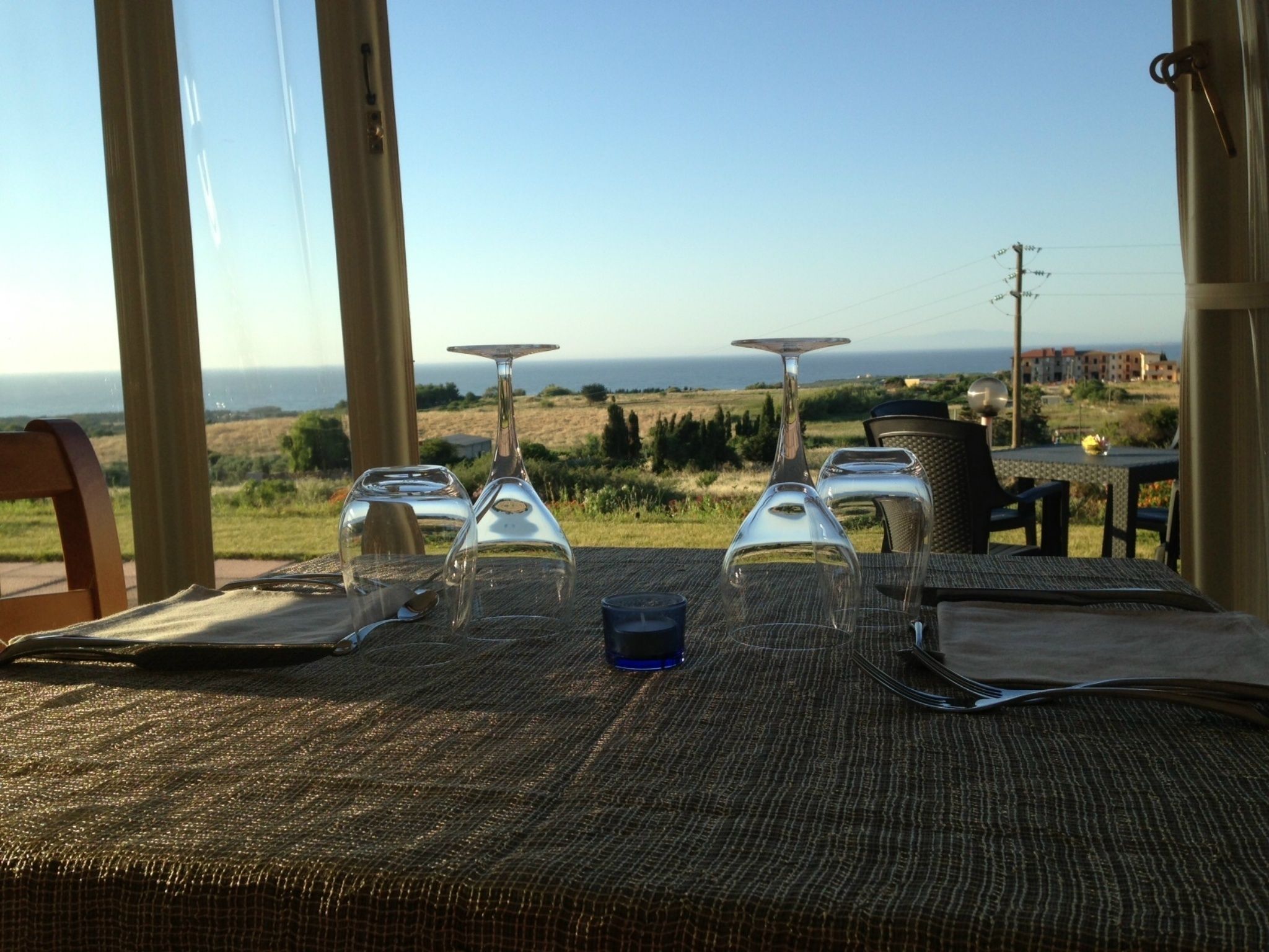 A table set for dining with wine glasses and a blue glass, overlooking a scenic view of the sea and landscape.