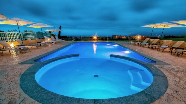 Una piscina con sillas de descanso y sombrillas, rodeada por una terraza de piedra.