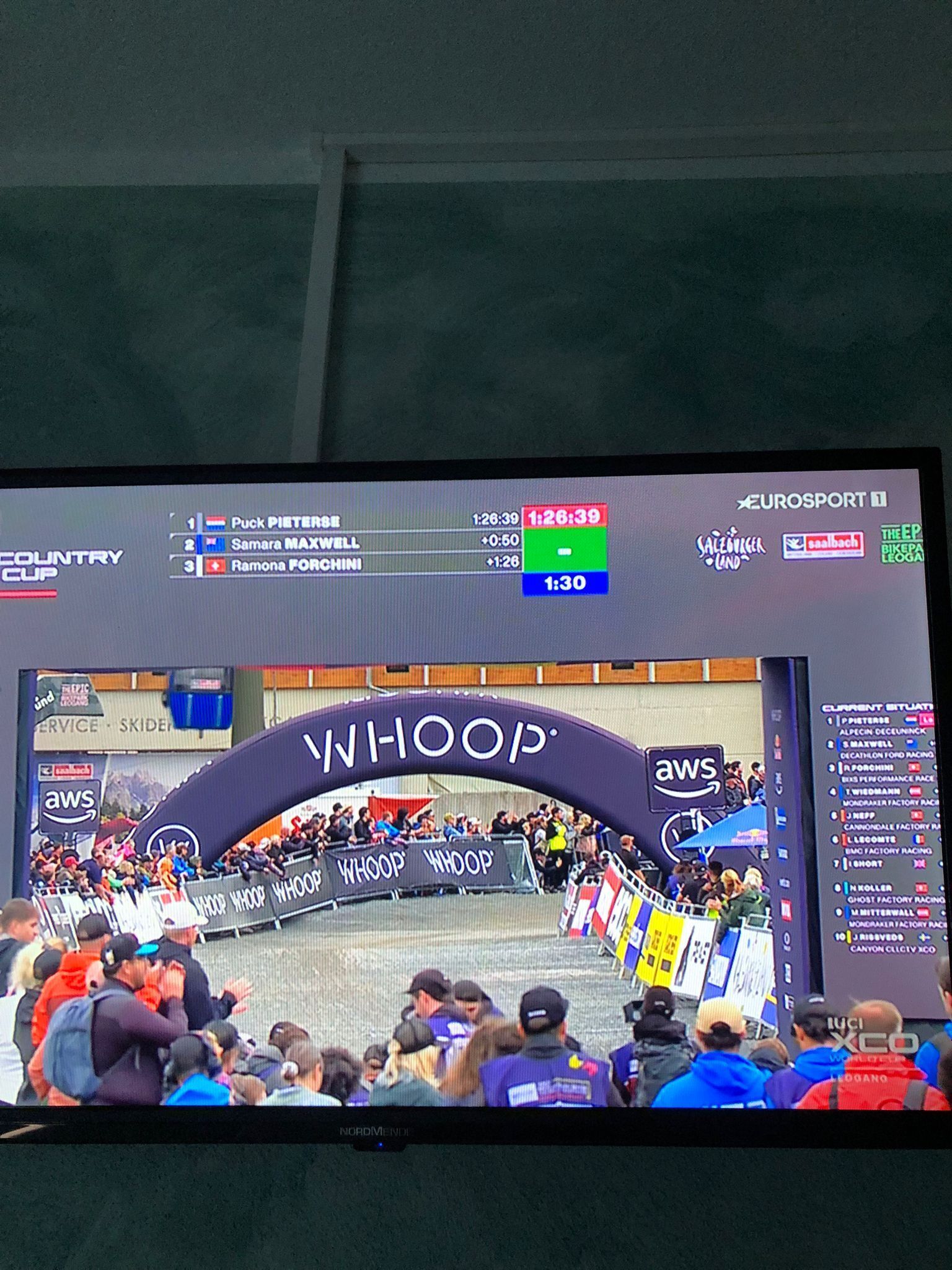Una pantalla de televisión mostrando un evento de ciclismo con un podio y público.