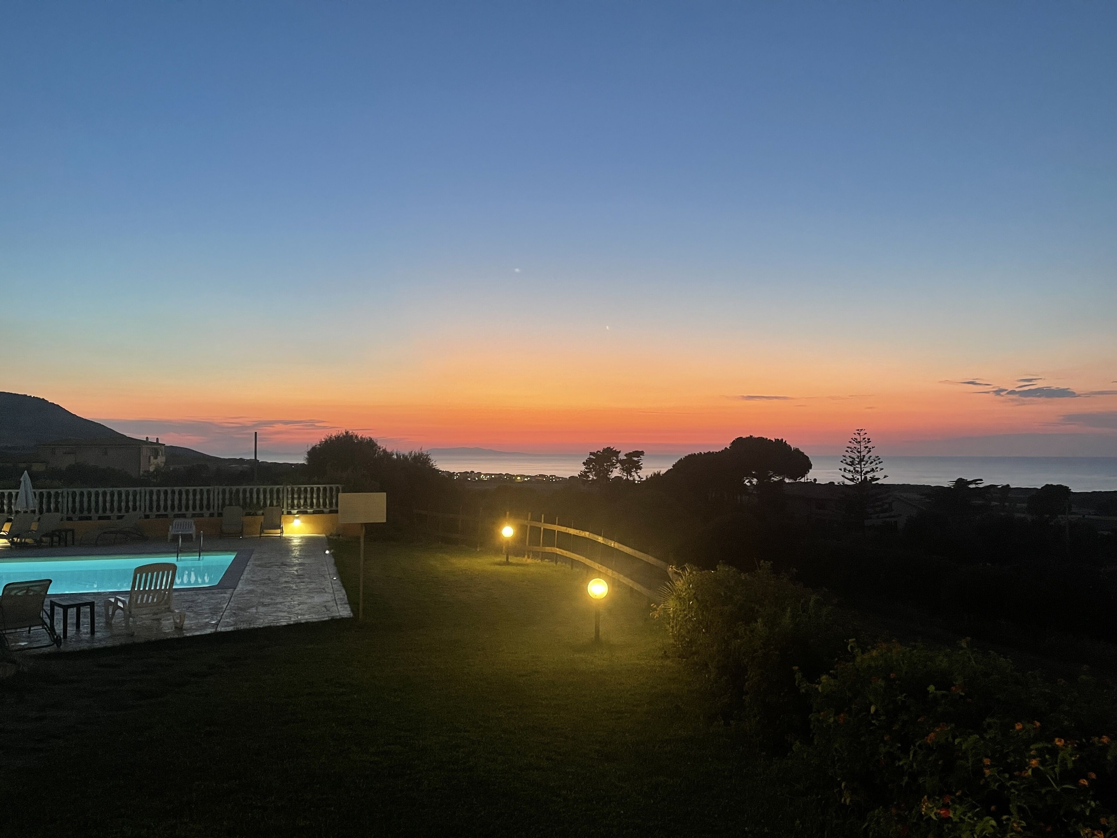A pool area with a sunset view, a pathway, and a distant mountain.