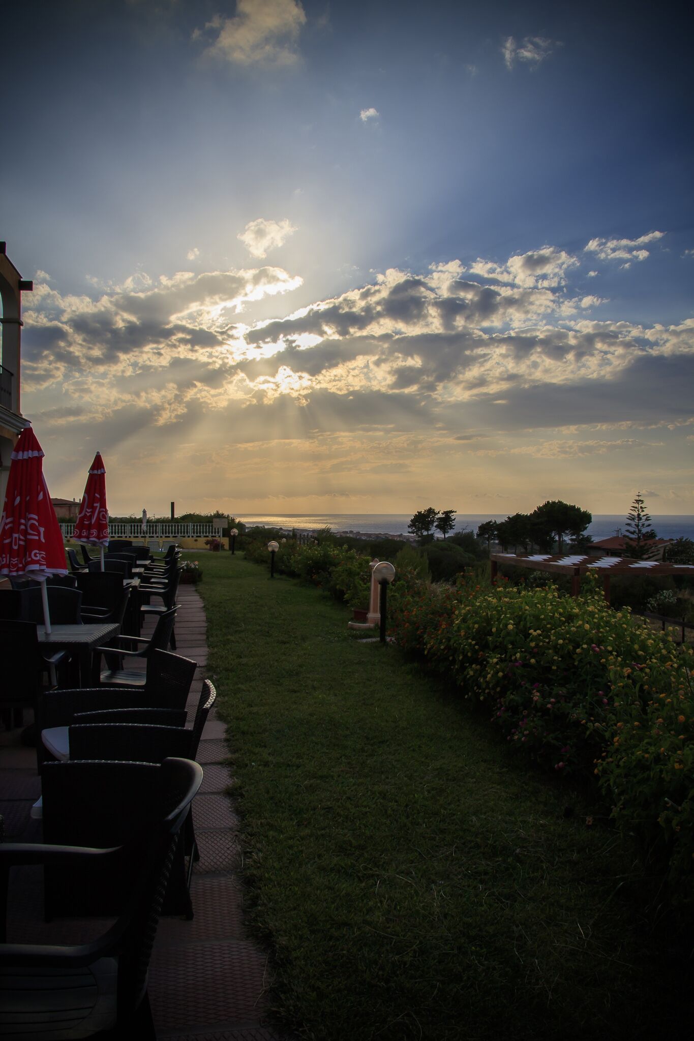 An outdoor seating area with tables and chairs, a pathway, and a view of the sea.