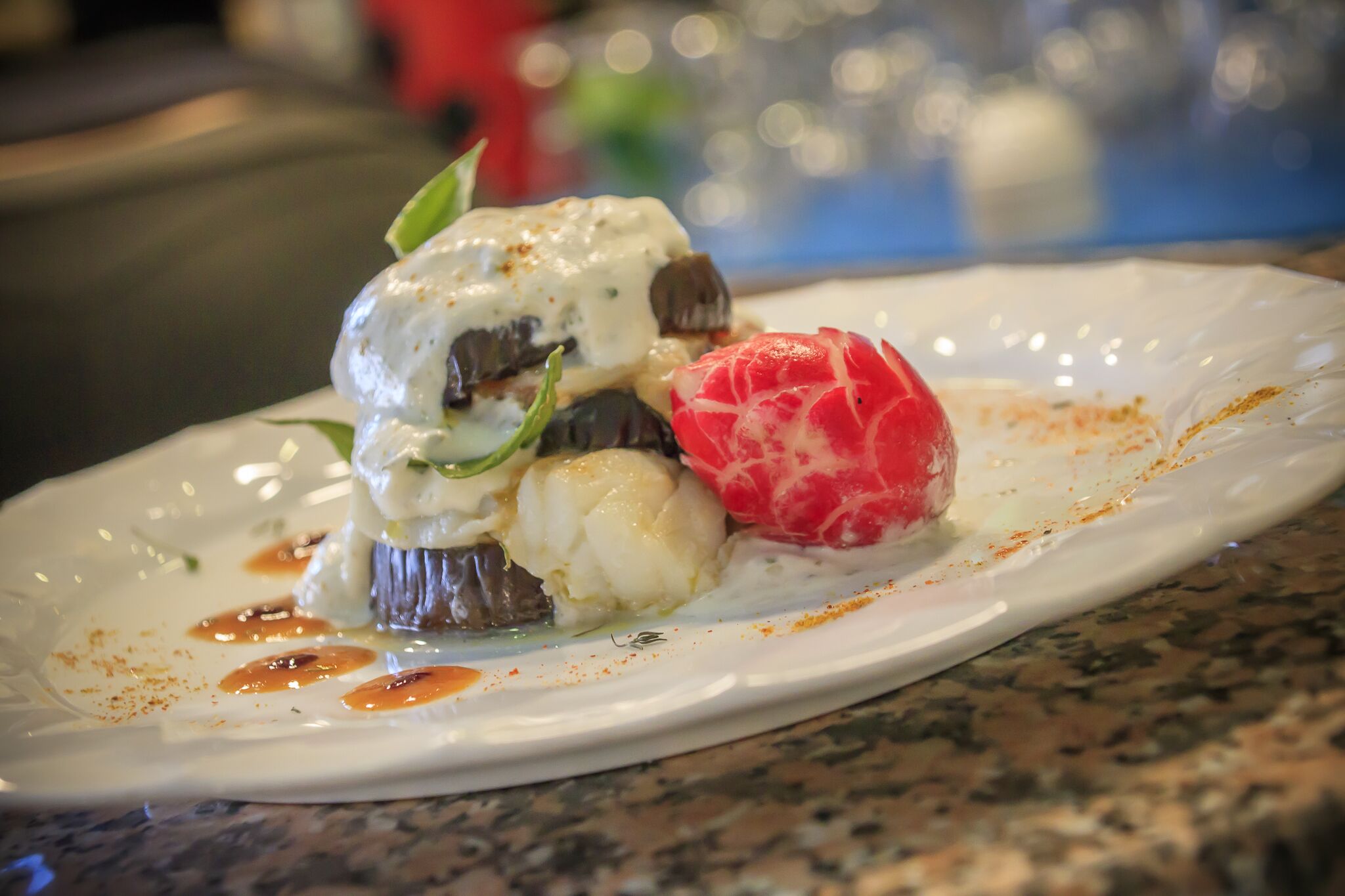 Un plato con un postre que incluye una esfera blanca, una fruta roja y una esfera blanca con salsa.