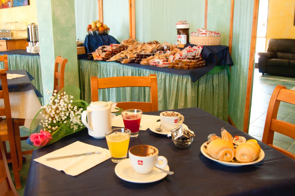 A breakfast setting with a table set for two, featuring a variety of pastries, a coffee cup, a glass of orange juice, and a floral arrangement.