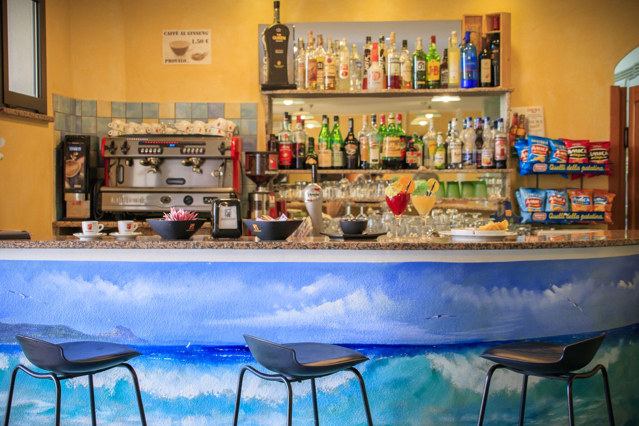 A bar area with a coffee machine, shelves of liquor bottles, and bar stools.