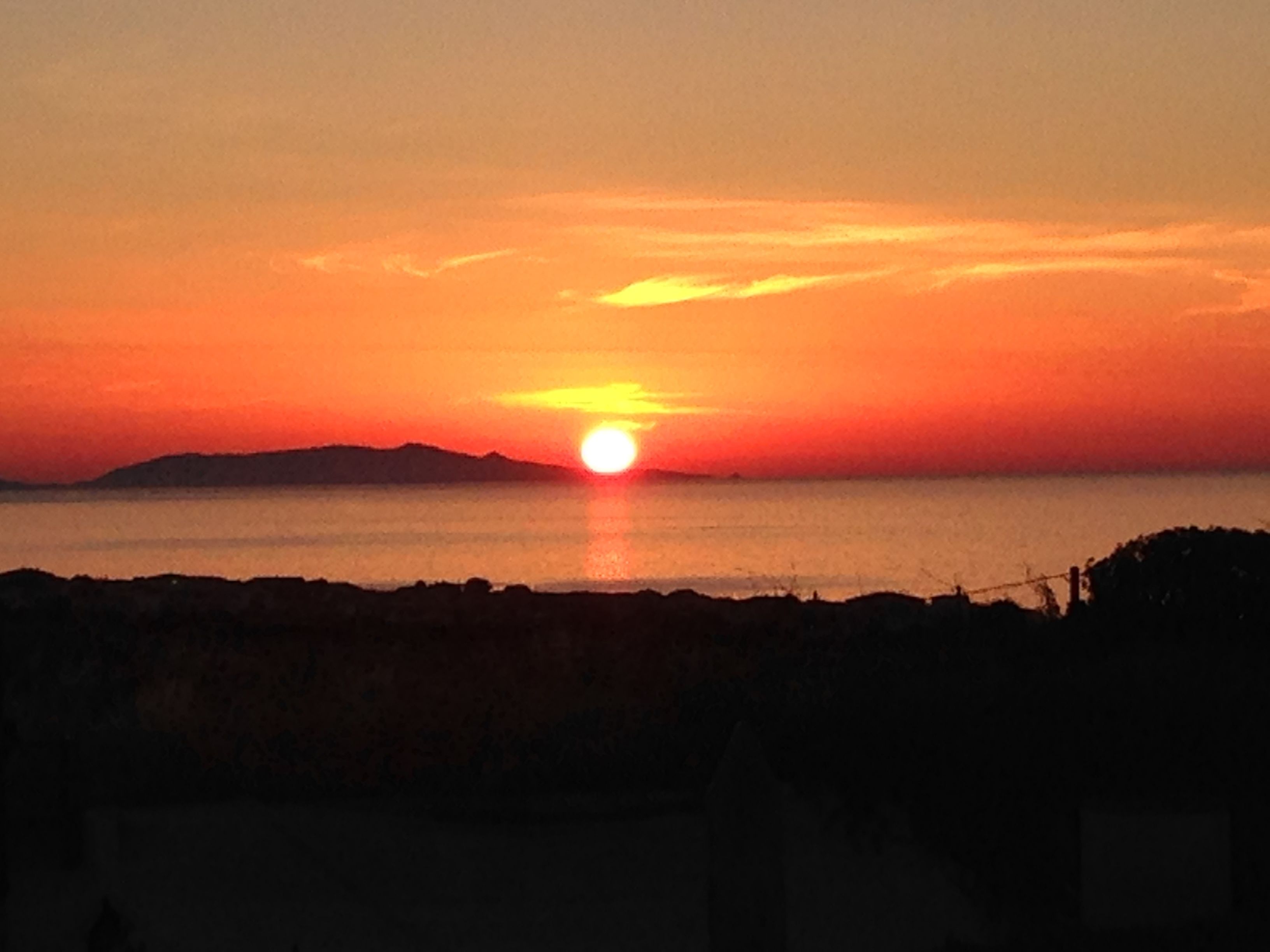 A sunset over a body of water with a silhouette of land in the foreground.