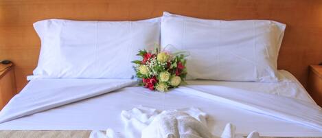 A neatly made bed with white linens, a bouquet of flowers, and a folded towel on a textured beige bedspread.