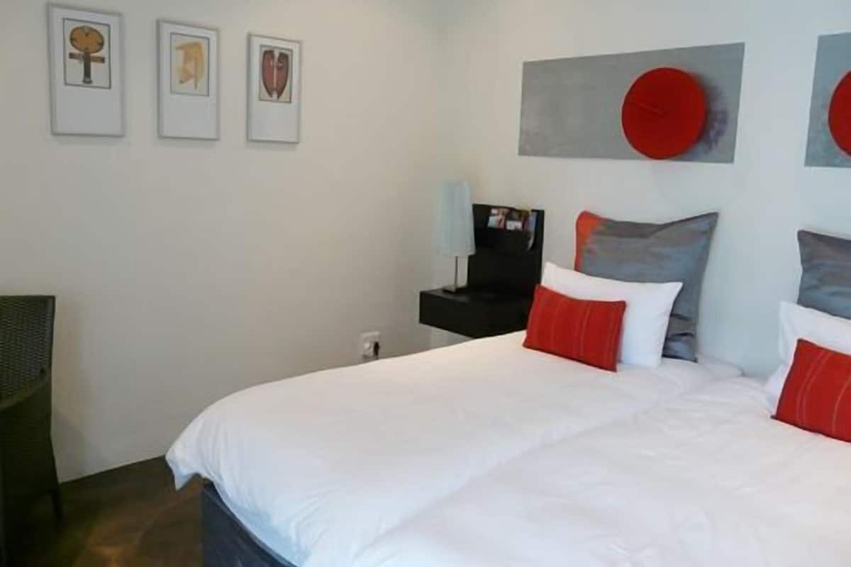 A modern bedroom with a large bed, a nightstand, and three framed artworks on the wall.
