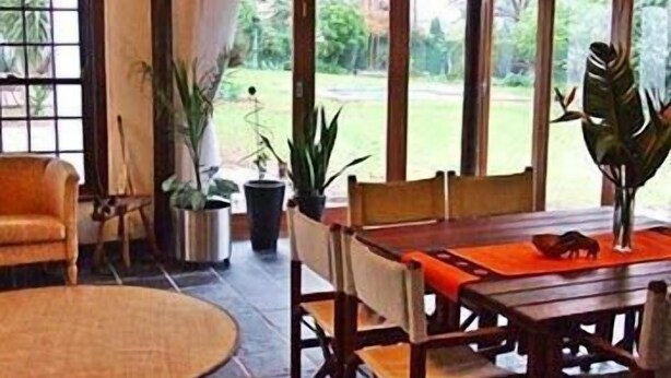 A dining area with a wooden table and chairs, surrounded by large windows offering a view of a garden. - KaapsePracht (Cape Town)