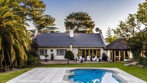 A house with a swimming pool, a patio with chairs, and a thatched-roof structure. - KaapsePracht (Cape Town)