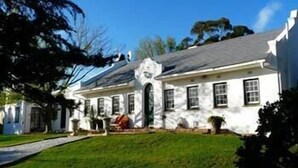A white two-story house with a sloped roof, a front porch, and a well-maintained lawn. - KaapsePracht (Cape Town)