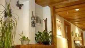A hallway with wooden beams, potted plants, and wall-mounted decorations. - Hotel Post Hardermannli (Unterseen)