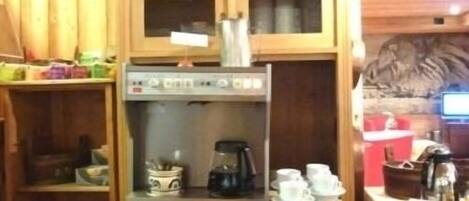 A wooden kitchen with a coffee machine, tea pots, and cups on shelves.
