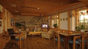 A cozy room with a wooden ceiling, a large mural, a TV, and a dining area with chairs and a table. - Hotel Post Hardermannli (Unterseen)
