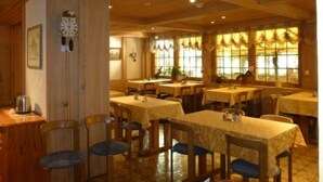 A dining area with wooden tables and chairs, a clock on the wall, and large windows with curtains. - Hotel Post Hardermannli (Unterseen)