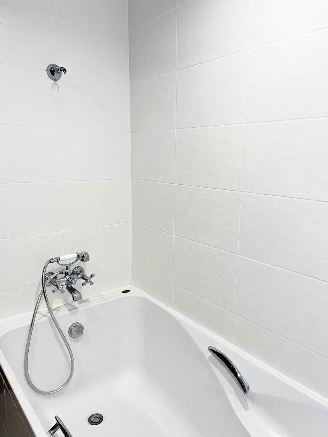 A modern bathroom with a freestanding bathtub, a handheld showerhead, and a wall-mounted faucet.