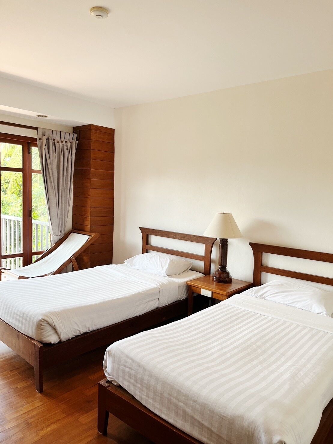 A hotel room with two single beds, wooden headboards, a wooden floor, and a window with curtains.