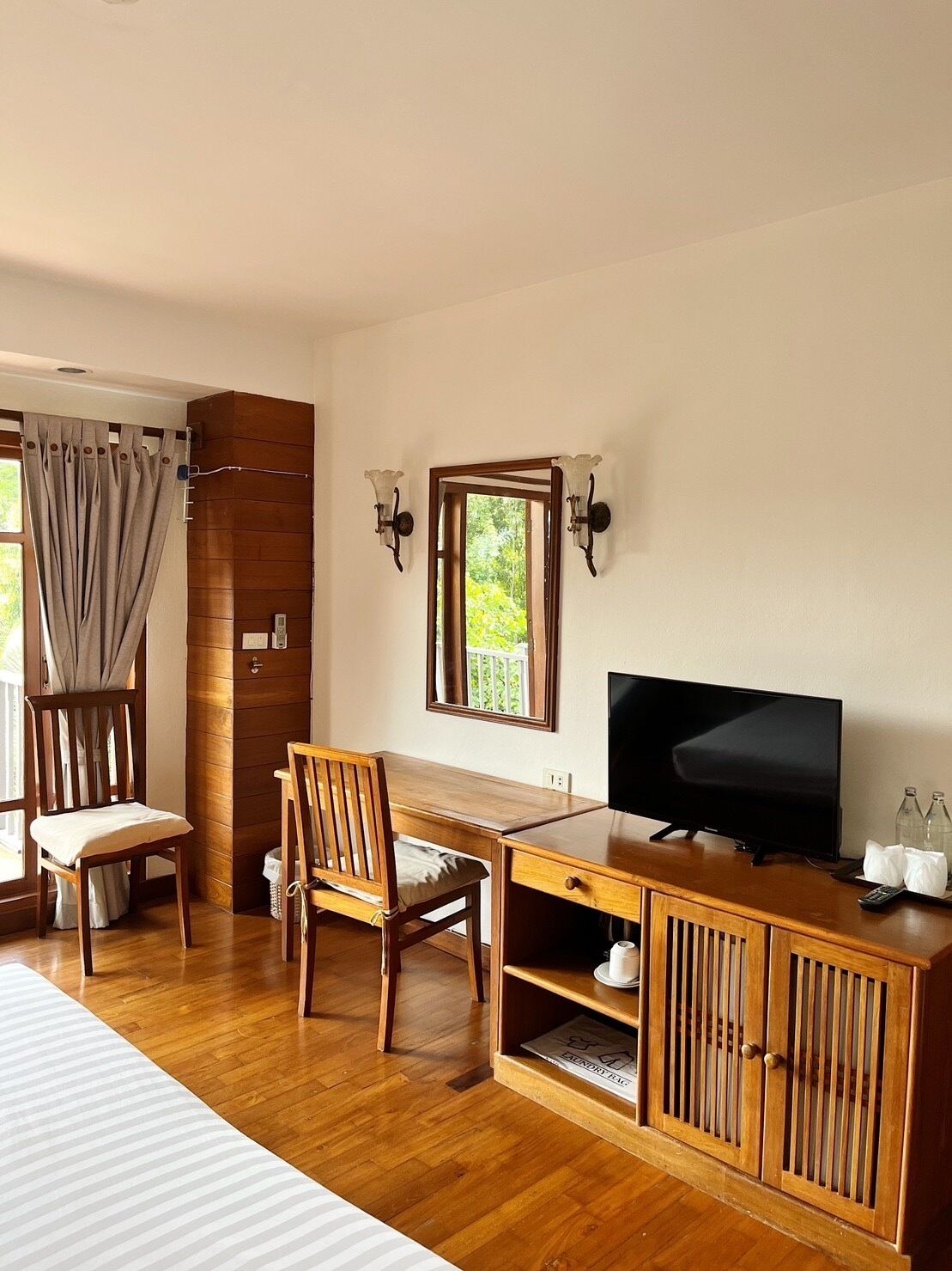 Habitación de hotel con una mesa de comedor de madera, dos sillas, un televisor y un mueble con un espejo arriba.