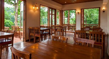 Un comedor amplio con mesas y sillas de madera, grandes ventanales con vistas al entorno verde.