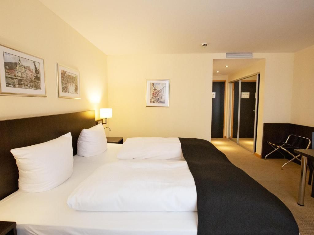 A hotel room with a bed, a desk, and a chair. There are framed pictures on the wall.