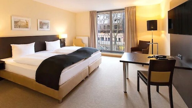 A hotel room with a large bed, a desk, a chair, and a TV. - DORMERO Hotel Altes Kaufhaus Lüneburg (Lueneburg)