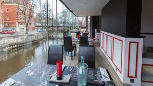 A restaurant with a view of a canal, modern interior design, and a menu on the table. - DORMERO Hotel Altes Kaufhaus Lüneburg (Lueneburg)