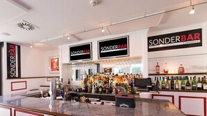 A bar area with multiple 'Sonderbar' signs, a well-stocked bar counter, and a variety of liquor bottles. - DORMERO Hotel Altes Kaufhaus Lüneburg (Lueneburg)