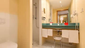 A bathroom with a toilet, a shower, a sink with a mirror, and a towel rack.
