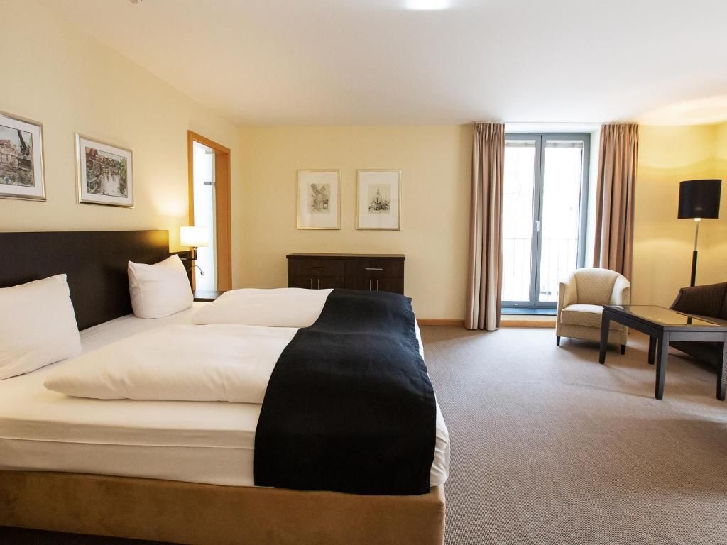 A hotel room with a large bed, a desk, a chair, and a window with curtains.