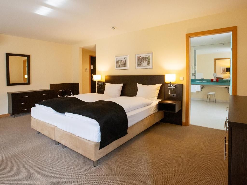 Ein Hotelzimmer mit einem großen Bett, Nachttischen, einem Schreibtisch und einem Spiegel.