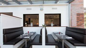 Un ristorante moderno con sedute in pelle nera e tavoli rettangolari, un soffitto in vetro e una parete in mattoni.