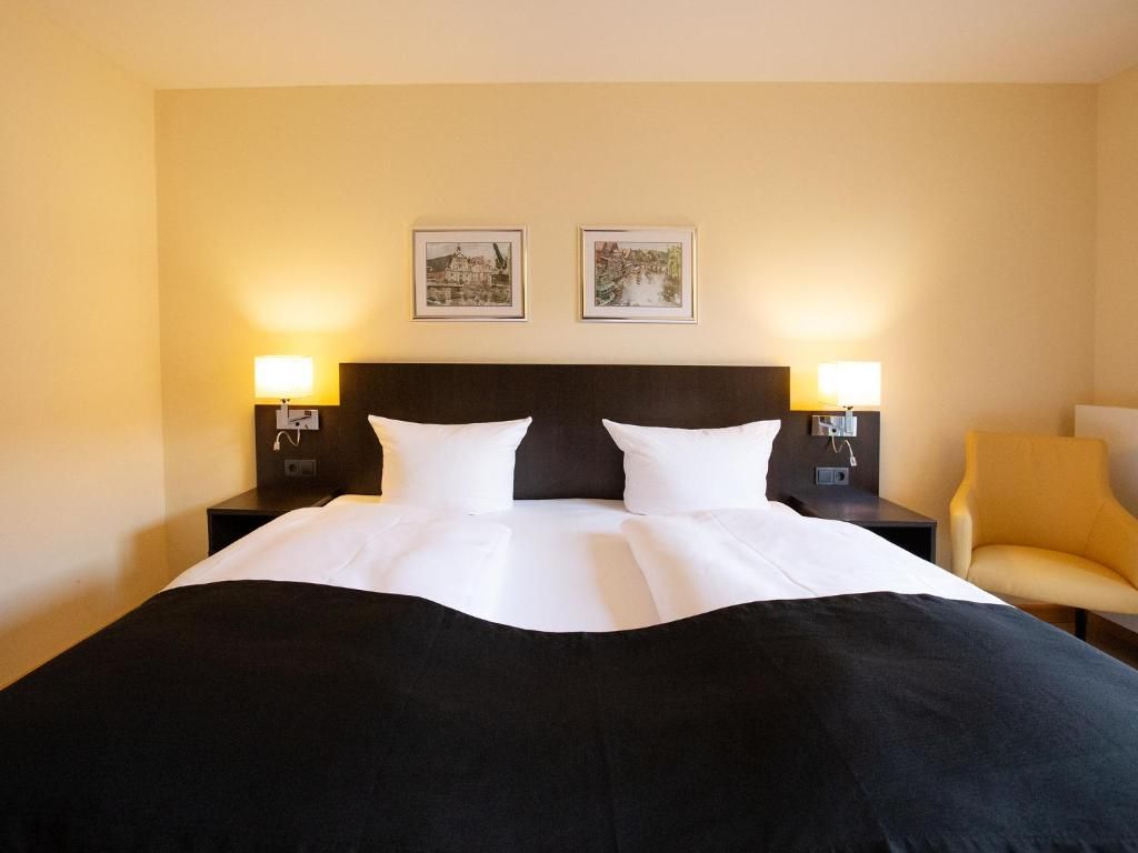 Une chambre d’hôtel avec un grand lit, deux tables de chevet avec des lampes, une chaise et deux tableaux encadrés au mur.